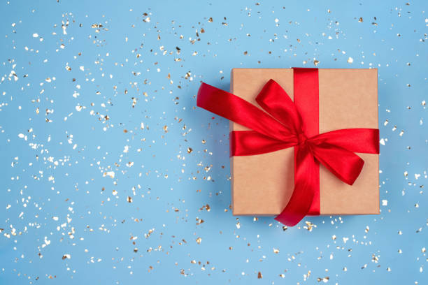 istock Gift box with red bow on festive blue background with golden sparkles around and copyspace for your text. Flat lay style. Christmas, New Year, Valentines Day or birthday celebration concept 1283383606