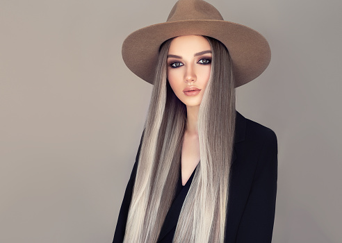 Portrait of young attractive woman dressed in a cowboy style hat. Nicely looking model with long,straight hair, dyed in a pale gray shade with the blonde wisps. Perfect model straightly gazing at the viewer. Beauty, elegance and hairstyling.