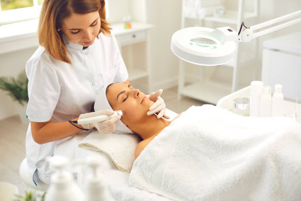 Smiling dermatologist making skincare procedure ultrasound Microdermabrasion for woman in beauty salon Microdermabrasion skincare in beauty salon. Smiling woman dermatologist making skincare procedure of ultrasound Microdermabrasion with special metal machine for relaxing young woman microdermabrasion stock pictures, royalty-free photos & images