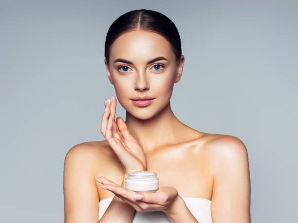 Cute woman applying cream to her face Cute woman applying cream to her face beautician stock pictures, royalty-free photos & images