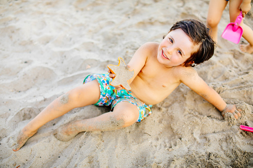 Happy laughing toddler boy having fun on sand
