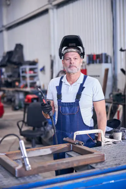 Photo of Bearded male worker using welding torch in garage