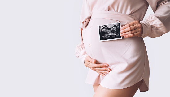 Pregnant woman holding ultrasound baby image. Close-up of pregnant belly and sonogram photo in hands of mother. Concept of pregnancy, gynecology, medical test, maternal health.