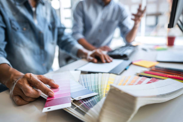 istock Two colleagues creative graphic designer working on color selection and drawing on graphics tablet at workplace, Color swatch samples chart for selection coloring 1283414315