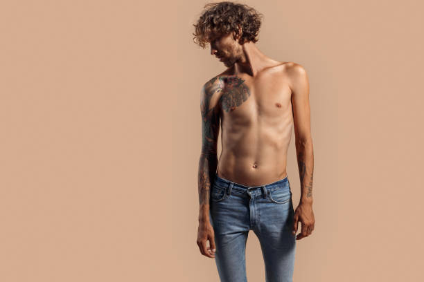 freestyle. hombre con el pelo rizado y la parte superior del cuerpo desnuda en jeans de pie aislado en beige mirando a un lado sensual - stubble men tattoo sensuality fotografías e imágenes de stock