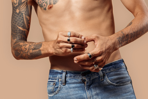 Man with bare upper body studio standing isolated on beige background touching fingers wearing rings