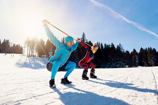 Caucasian ethnicity man and woman exercising before skiing at ski slope on a beautiful sunny day.
