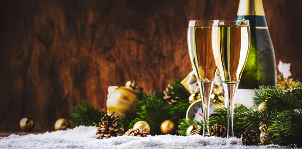 Two champagne glasses and christmas decoration on wooden snow golden bokeh background. Happy New Year Celebration. Selective focus and small depth of field