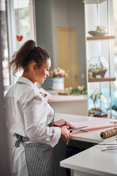 istock Professional flower shop worker cutting paper for wrapping a bouquet 1283416515