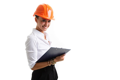 Beautiful caucasian female in office clothes write notes and holds an orange construction helmet isolated on white background.