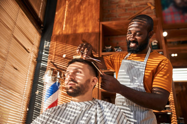 istock Smiling barber cutting client hair with scissors in barbershop 1283421580