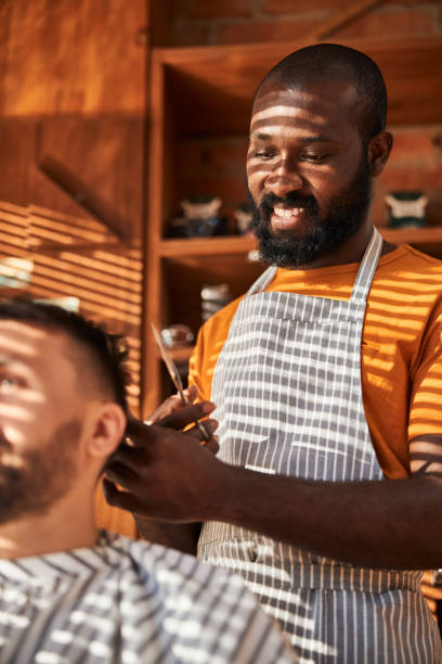 istock Smiling barber making haircut for client in barbershop 1283421584