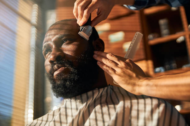 istock Male barber trimming client beard in barbershop 1283421644