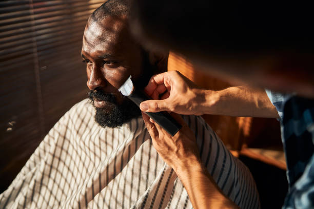 istock Barber shaving client beard with electric trimmer in barbershop 1283421647