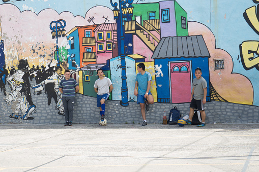 Buenos Aires, Argentina.  November 2, 2019:   A group of street soccer players in La Boca district resting against the wall with an interesting cityscape mural.