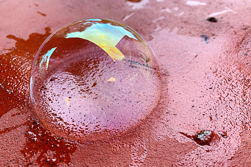 The soap bubble lies on a red brick surface. Transparent soapy surface with rainbow colors and reflections