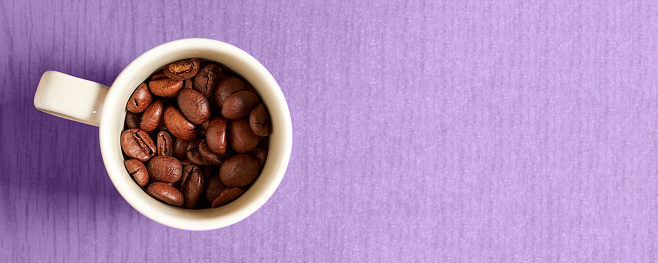 Espresso mug with roasted coffee beans on the purple surface with copy space. Flat lay food and drink design with free space for advertisement text