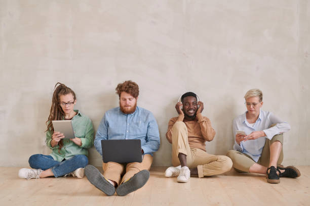 istock Different young multi-ethnic people sitting on floor and using modern devices such as gadgets and laptop 1283436279