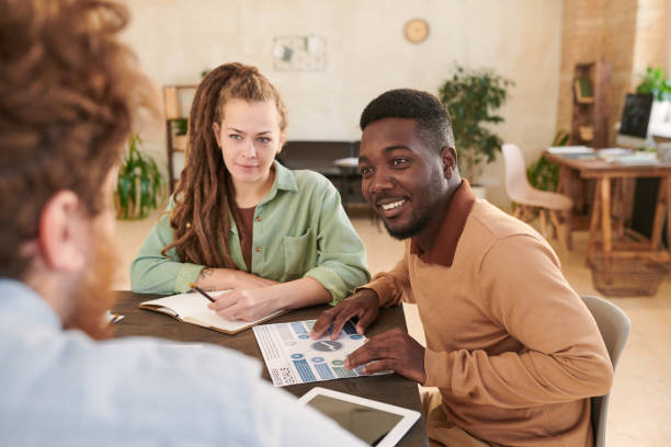 istock Smiling young African-American marketer listening to colleagues idea while they collaborating in modern office 1283436344