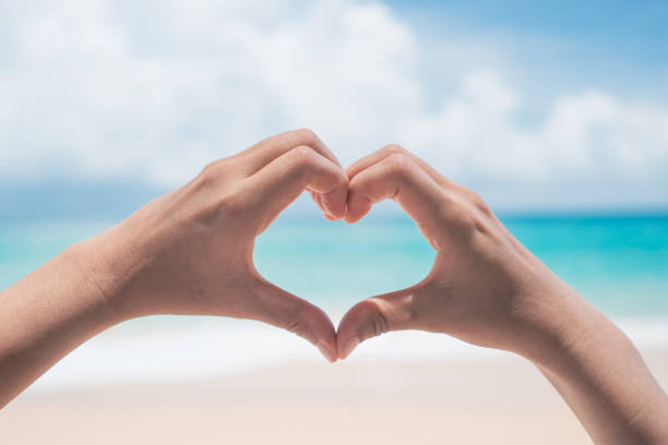 istock Woman hand do heart shape on blue sky and beach background. 1283437870