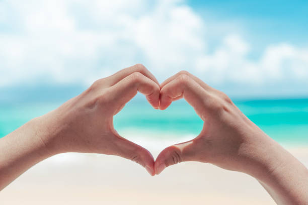 istock Woman hand do heart shape on blue sky and beach background. 1283437877
