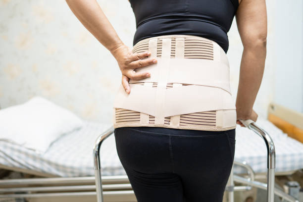 patient asiatique de dame utilisant la ceinture de soutien de douleur dorsale pour lombaire orthopédique avec le marcheur. - orthèse photos et images de collection