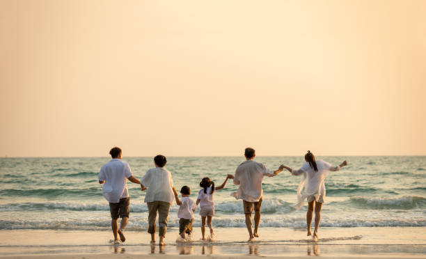 glückliche mehrgenerationen-asiatische familie hält hände und geht am strand zusammen bei sonnenuntergang im sommer. lächelnde große familie eltern mit kind junge und mädchen genießen im freien lifestyle-reiseurlaub - family grandmother multi generation family nature stock-fotos und bilder