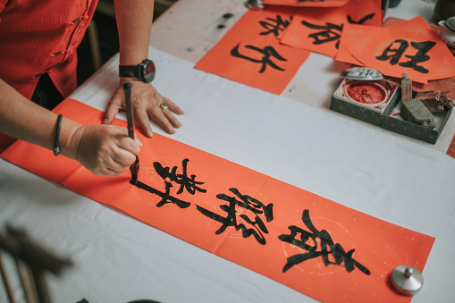 hand of asian chinese male practising chinese caligraphy for coming chinese new year celebration home decoration purpose with prosperity and good wording by writing it on a red piece of paper