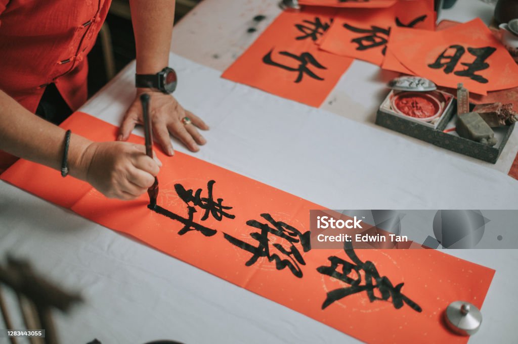 hand of asian chinese male practising chinese caligraphy for coming chinese new year celebration home decoration purpose with prosperity and good wording by writing it on a red piece of paper 55-59 Years Stock Photo