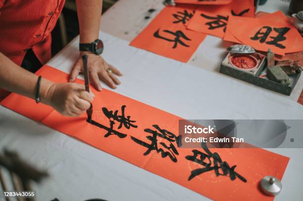 Hand Of Asian Chinese Male Practising Chinese Caligraphy For Coming Chinese New Year Celebration Home Decoration Purpose With Prosperity And Good Wording By Writing It On A Red Piece Of Paper Stock Photo - Download Image Now