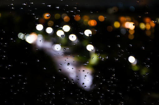 Raindrops on window glass and night lights bokeh background. Blurred lights. Abstract rain background
