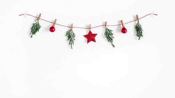 Photo of Christmas composition. Garland made of red balls and fir tree branches on white background. Christmas, winter, new year concept. Flat lay, top view