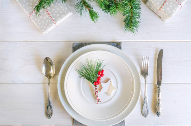 istock Christmas table setting with traditional Christmas decoration in white red tone. Beautiful festive dinner background. Xmas tableware, plate with linen napkin and vintage cutlery, green fir branch and red berries 1283461559