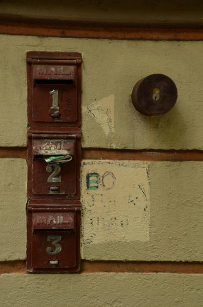 istock Three old mail boxes aligned vertically in yellow brick wall. Numbered 1, 2, 3. Faded painted words and lock in circular barrel next to boxes. 1283463817