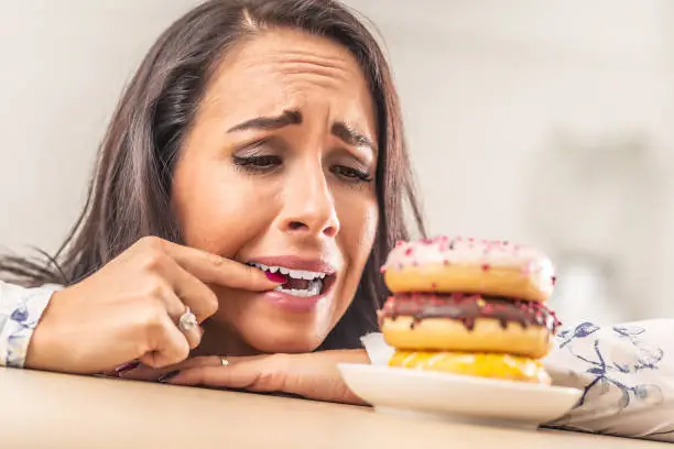 Photo of Female desperately trying to resist donuts, biting her finger.