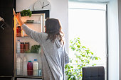 Woman by the open fridge taking a bunch of parsley