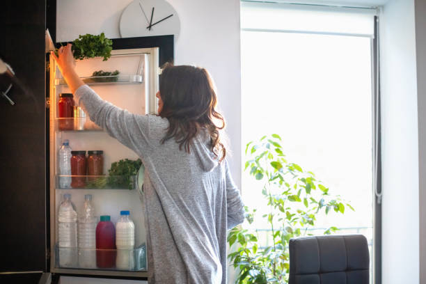 Woman by the open fridge taking a bunch of parsley Woman holding the fridge door and taking a bunch of parsley refrigerator photos stock pictures, royalty-free photos & images