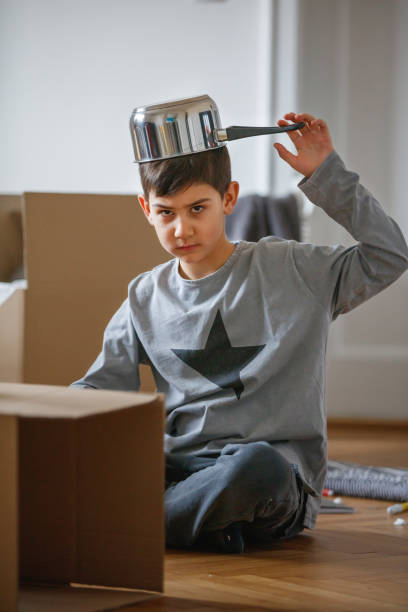 istock Boy on the floor amid cardboard boxes with cooking pan on his head 1283471398