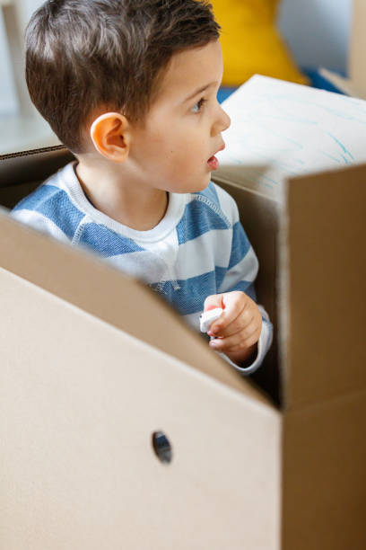 istock Boy sitting in empty box and holding a piece of packing peanut 1283471424
