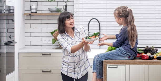 mãe e filha felizes prepararam salada vegetal. conceito de comida saudável. - mother green sparse contemporary - fotografias e filmes do acervo