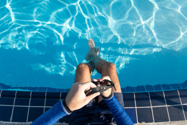 istock Man holding swimming goggles by the pool on a sunny day 1283474876