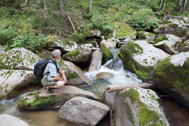 istock Man with a backpack sitting on a stone near a mountain river on a summer day, Belokurikha River, Belokurikha City, Altai Mountain 1283475324