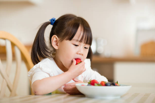 młoda dziewczyna jedząca truskawkę na prawdziwym tle kuchni - juicy childhood colors red zdjęcia i obrazy z banku zdjęć