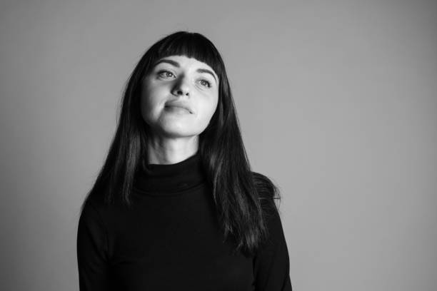 close up studio portrait of a young woman against plain grey background - black and white portrait people women imagens e fotografias de stock