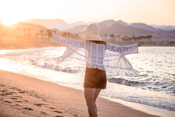 istock A woman in a hat walks at sunset on the beach rear view 1283477550