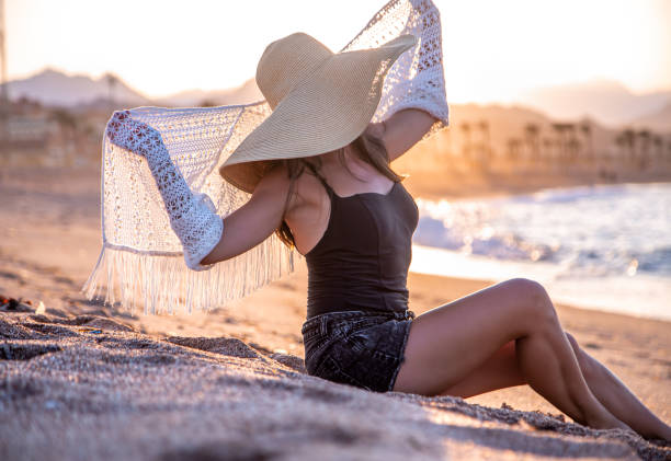 istock Beautiful boho model in a hat poses on the beach in the sun 1283477551