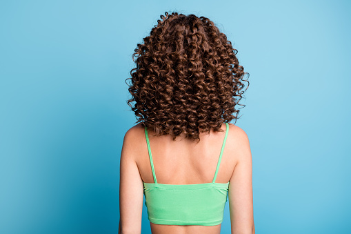 Rear back photo of young lady stand big extensive volume hairstyle, nice curls sporty athletic trained spine back after exercises wear green crop top isolated blue color background