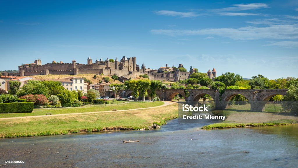 Carcasonne Cityscape Panorama in Summer France Carcasonne cityscape panorama view over aude river in summer under blue sunny sky. Medieval fortified stone wall on hill top, Pont Vieux old stone bridge crossing the Aude river on the left. Carcasonne, Languedoc Rousillon, South France, France, Europe. Carcassonne Stock Photo