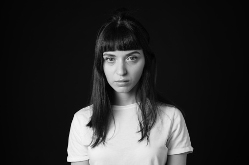 Studio portrait of a pretty brunette woman in a white blank t-shirt, against a plain black background, seriouly looking at camera