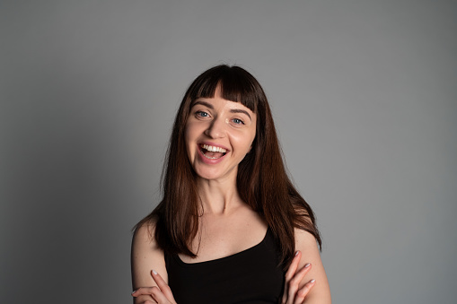 Studio portrait of a pretty smiling woman, wearing spaghetti strap top, looking at the camera, against a plain grey background